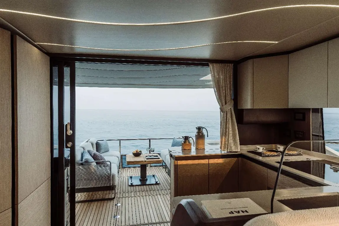 Luxurious yacht interior with a view of the sea, featuring a dining area, kitchen, and outdoor seating.